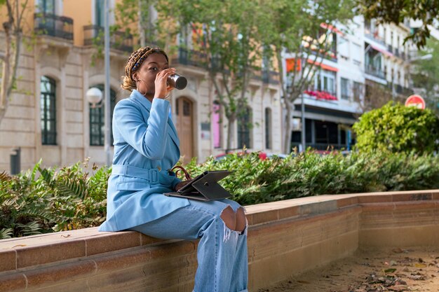 Schwarze Geschäftsfrau arbeitet remote in einem Park einer Stadt mit einem Touch-Laptop und trinkt Kaffee
