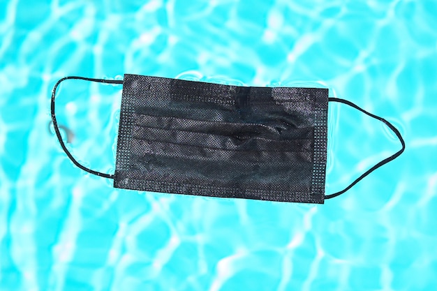 Schwarze Gesichtsmaske zum Schutz vor dem Corona-Virus (COVID-19) im Schwimmbadwasser.