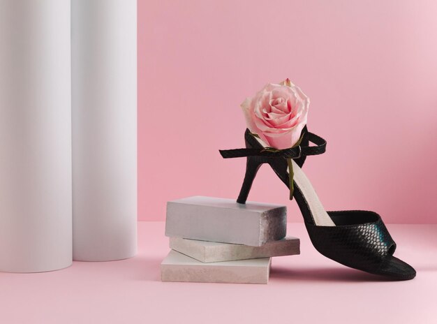 Schwarze High Heels und rosa Rosenblüte auf pastellrosa Hintergrund Minimales nachhaltiges Modekonzept