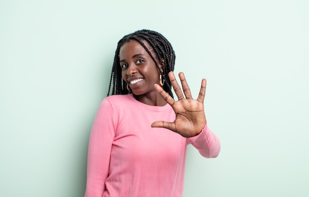 Schwarze hübsche Frau, die lächelt und freundlich aussieht, die Nummer fünf oder fünf mit der Hand nach vorne zeigt und herunterzählt