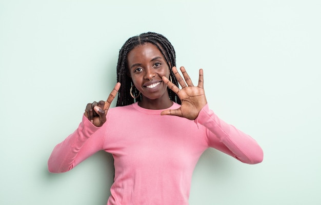 Schwarze hübsche Frau, die lächelt und freundlich aussieht, die Nummer sechs oder sechs mit der Hand nach vorne zeigt und herunterzählt