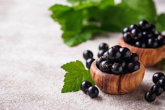 Schwarze Johannisbeere mit Blättern in hölzernen Schüsseln