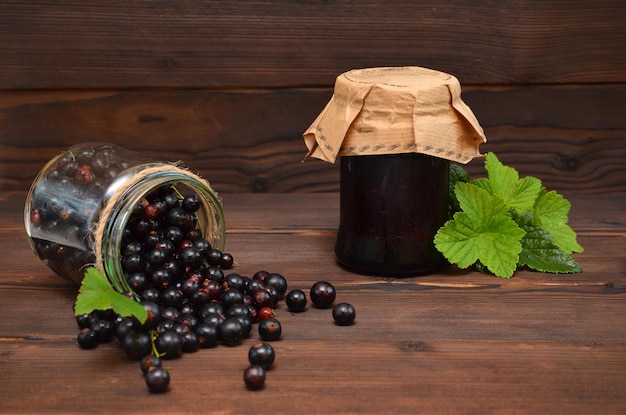 Schwarze Johannisbeere verschüttet auf dem Tisch und ein Glas Beerenmarmelade