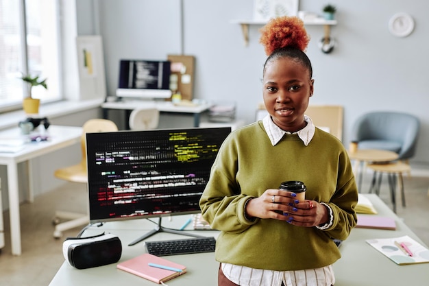 Schwarze junge Frau als Softwareprogrammiererin, die im Büro in die Kamera lächelt