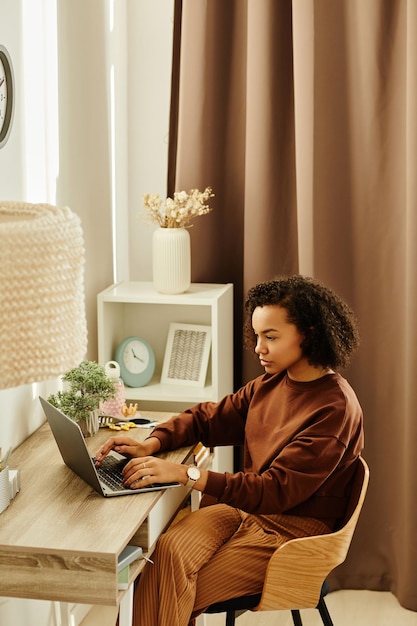 Schwarze junge Frau benutzt Laptop in gemütlichem Zuhause