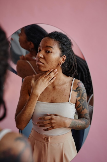 Schwarze junge Frau mit Aknenarben, die unsicher im Spiegel aussieht