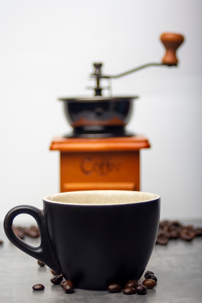 schwarze Kaffeetasse mit Kaffeebohnen fiel neben einer Kaffeemühle Hintergrund.