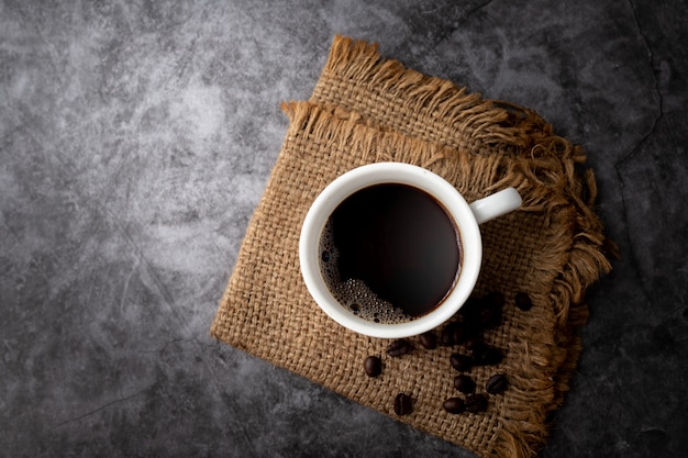 Schwarze Kaffeetasse und Kaffeebohnen auf Zement