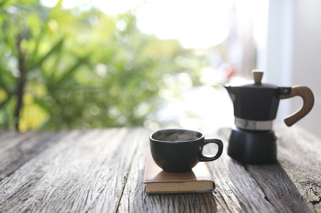 Schwarze Kaffeetasse und schwarze Mokkakanne mit Ledernotizbuch auf Holztisch