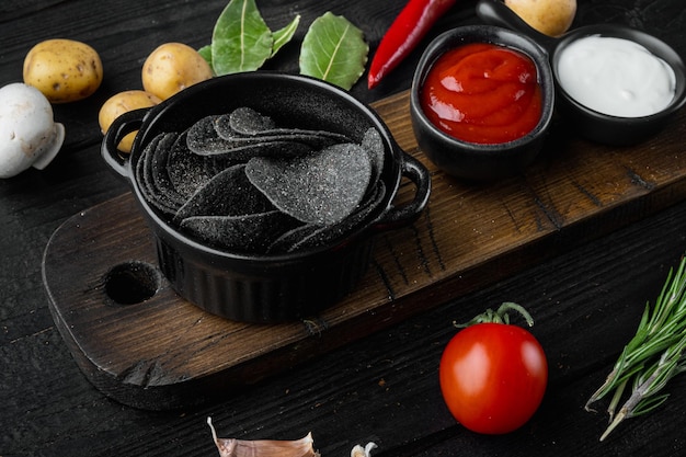 Schwarze knusprige Kartoffelchips auf schwarzem Holzhintergrund