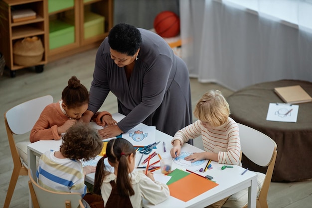 Schwarze Lehrerin hilft kleinen Kindern im Kunst- und Handwerksunterricht im Vorschulalter