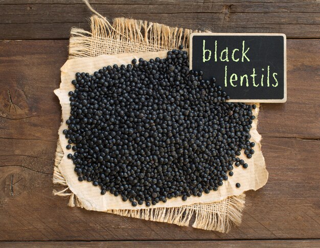 Schwarze Linsen mit einer kleinen Tafel auf Holz