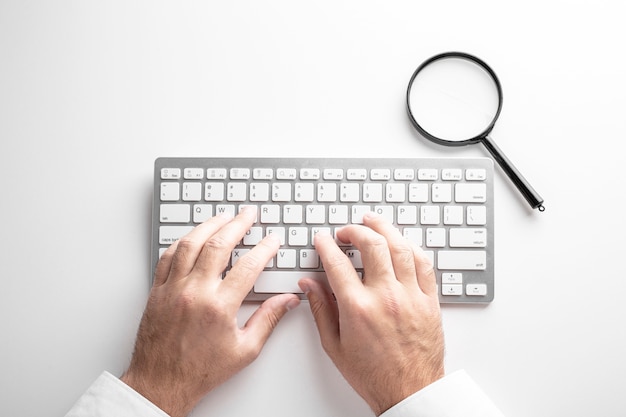 Foto schwarze lupe auf einer weißen tastatur auf einem weißen hintergrund. geschäftskonzept.