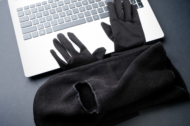 Schwarze Maske und schwarze Handschuhe auf einem Laptop