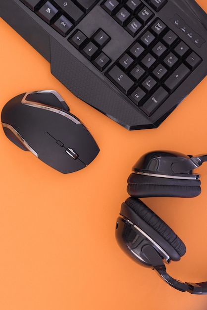 Schwarze Maus, Tastatur, Kopfhörer sind auf einem orangefarbenen Hintergrund isoliert, die Draufsicht.