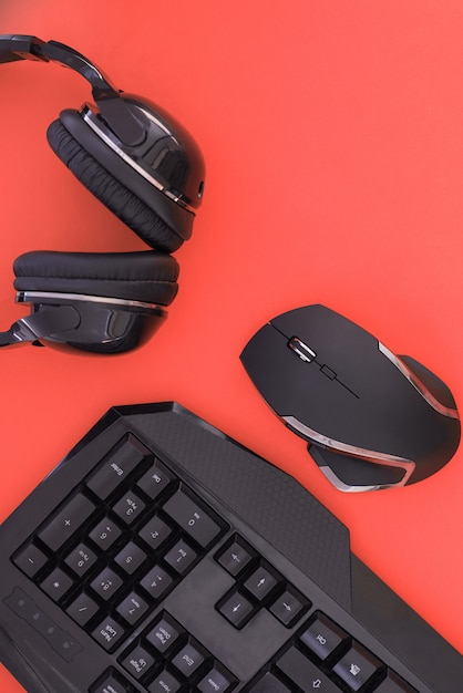 Schwarze Maus, Tastatur, Kopfhörer sind auf rotem Hintergrund isoliert, die Draufsicht. Flacher Spielerhintergrund