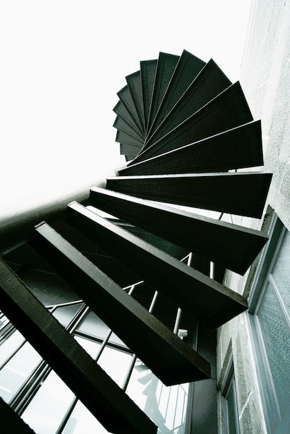 Foto schwarze metallaußenspindeltreppe mit gekörnter und geräuschbeschaffenheit auf weißem himmel, aufstiegswinkelsicht, steigern zum erfolgreichen und zielmeilenstein.