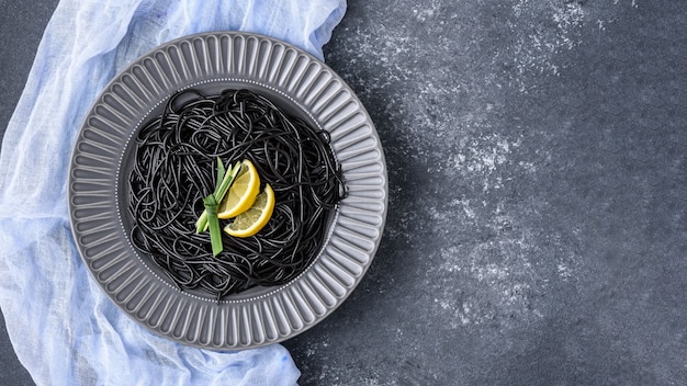 Schwarze Paste der Draufsicht mit Tinten-Tintenfisch und Zitronenscheiben in der grauen Platte