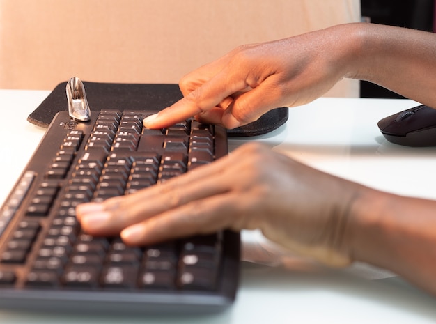 Schwarze Person tippt auf einer Tastatur auf einem weißen Tisch mit einem kleinen hochhackigen Schuh in der Ecke