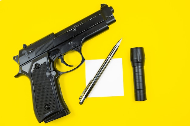 Schwarze Pistole, Erinnerungspapier, Stift und Taschenlampe liegen auf gelbem Hintergrund. Privatdetektive arbeiten. Suche nach Informationskonzept.