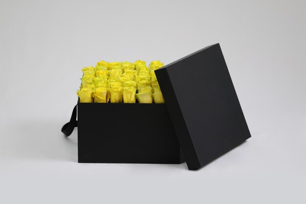 Schwarze quadratische Geschenk-Blumenverpackung mit gelben Rosen im Inneren und geöffnetem Deckel
