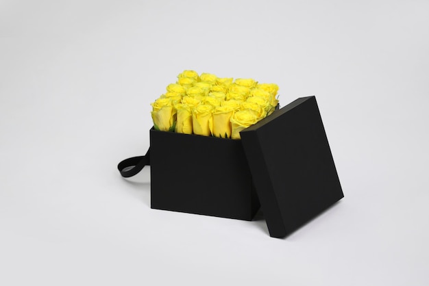 Schwarze quadratische Geschenk-Blumenverpackung mit gelben Rosen im Inneren und geöffnetem Deckel