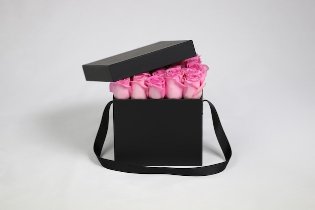 Schwarze quadratische Geschenk-Blumenverpackung mit rosa Rosen im Inneren und geöffnetem Deckel