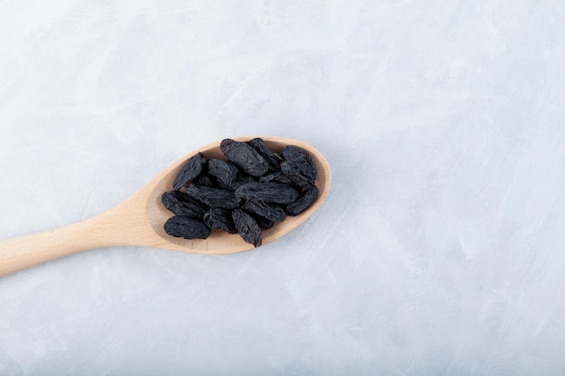 Schwarze rosinen in holzlöffel auf grauem hintergrund getrocknete dehydrierte traubenfrüchte