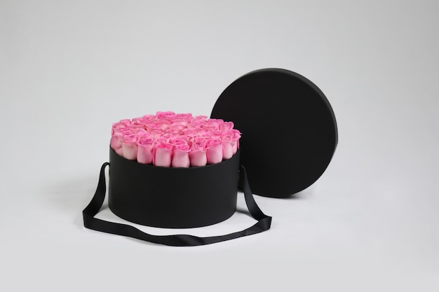 Schwarze runde Geschenk-Blumenverpackung mit rosa Rosen im Inneren und geöffnetem Deckel