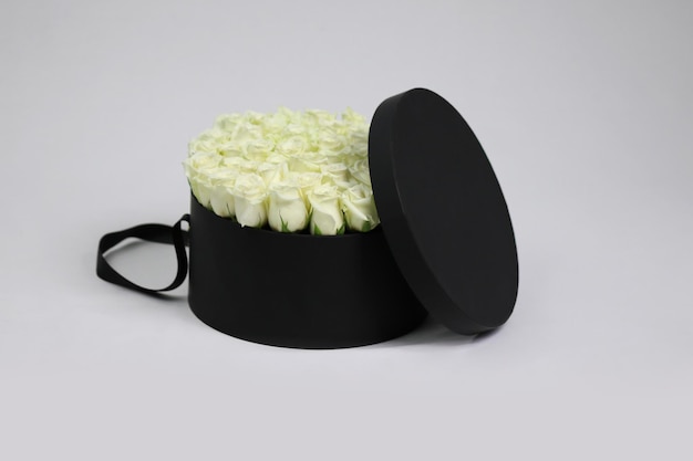 Schwarze runde Geschenk-Blumenverpackung mit weißen Rosen im Inneren und geöffnetem Deckel