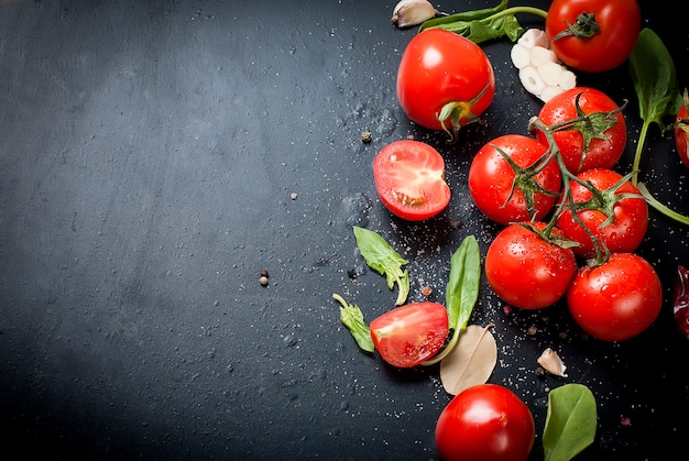 Schwarze rustikale Tischplatte mit Zweig der Tomaten und der Kräuter, Draufsicht