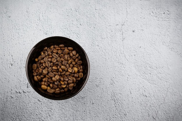 Schwarze Schüssel mit braunen Kaffeebohnen auf grauer Oberfläche, Ansicht von oben