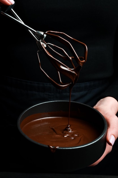Schwarze Schüssel mit dunkler heißer Schokolade in den Händen Küchenutensilien auf schwarzem Hintergrund
