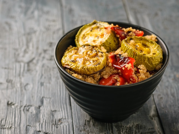 Schwarze Schüssel mit einem Salat aus gebackenem Gemüse und der gekochten Quinoa. Vegetarisches Gericht. Natürliche pflanzliche Nahrung. Der Blick von oben.