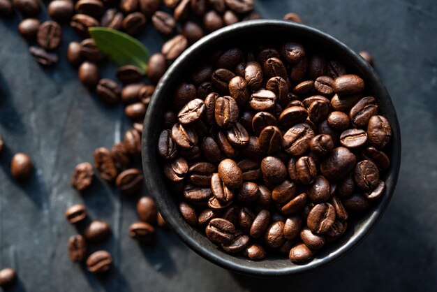 Schwarze Schüssel mit Kaffeebohnen, die auf dem dunklen Hintergrund-Draufsichtfensterfenster des Tisches verteilt sind