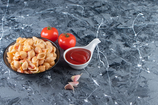 Schwarze Schüssel mit leckeren Muschelnudeln mit Ketchup auf Marmoroberfläche.