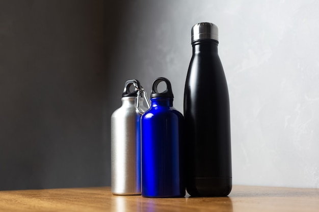 Schwarze, silberne und ultramarine Thermoflaschen auf Holztisch.