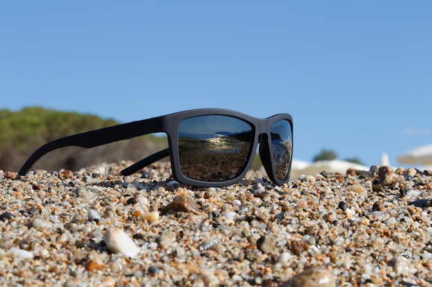 Schwarze Sonnenbrille auf Kiesel- und Himmelhintergrund