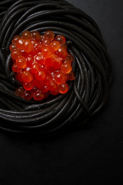 Schwarze Spaghetti mit roten Kaviar-Nudeln auf schwarzem Hintergrund Draufsicht keine Menschen