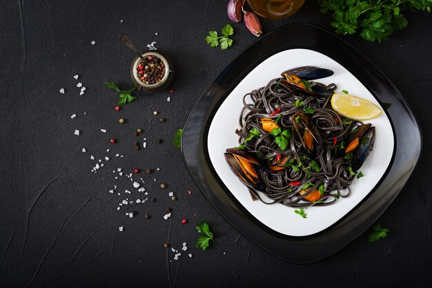 Schwarze Spaghetti. Nudeln mit schwarzen Meeresfrüchten mit Muscheln über schwarzem Tisch. Mediterrane Delikatesse. Flach liegen. Draufsicht