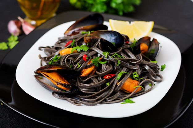 Schwarze Spaghetti. Nudeln mit schwarzen Meeresfrüchten mit Muscheln über schwarzem Tisch. Mediterrane Delikatesse