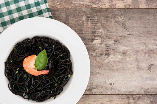 Schwarze Spaghettis mit Garnelen auf Holztisch.