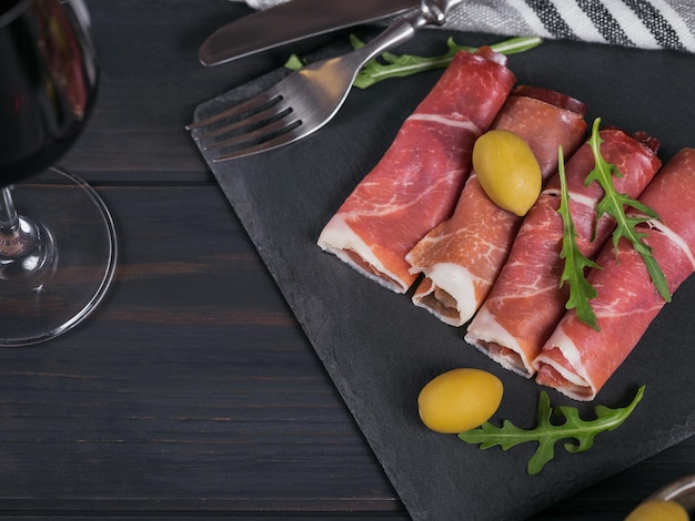 Schwarze Steinplatte mit Schinkenscheiben oder spanischem Jamon Serrano oder italienischem Prosciutto Crudo