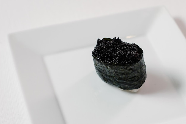 Schwarze Sushi-Maki-Rolle dekoriert auf Porzellanteller Copyspace