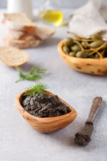 Schwarze Tapenade oder Tapas, traditionelles Gericht der Provence oder Dip mit Oliven und Basilikum auf einem alten Holztischhintergrund. Selektiver Fokus. Ansicht von oben