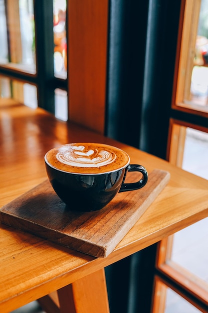 Schwarze Tasse Cappuccino mit Latte Art auf Holzhintergrund im Café