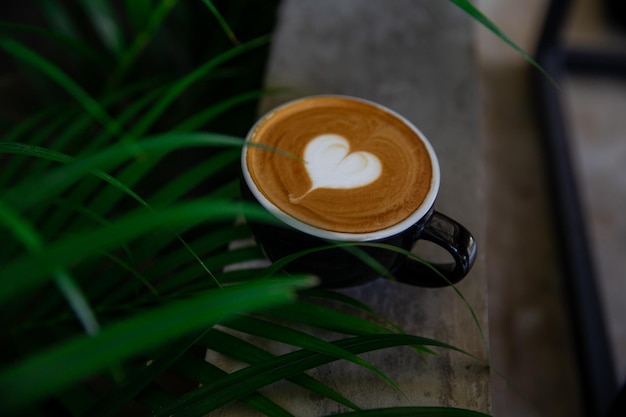 Schwarze Tasse Cappuccino mit Latte Art in Herzform auf Untertasse auf Betongrund