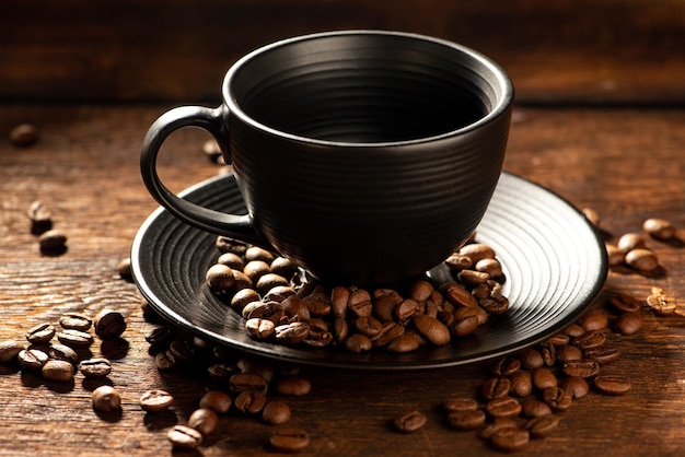 Schwarze Tasse schwarze Tasse mit Kaffeebohnen daneben auf selektivem Fokus des Fotos im rustikalen Holz im dunklen Lebensmittelstil