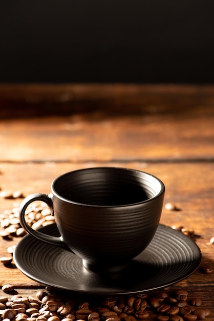 Schwarze Tasse schwarze Tasse mit Kaffeebohnen daneben auf selektivem Fokus des Fotos im rustikalen Holz im dunklen Lebensmittelstil