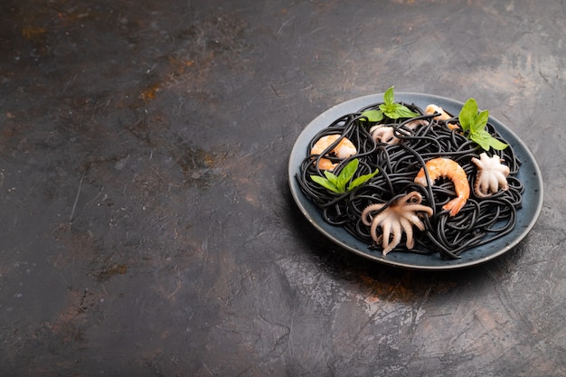 Schwarze Tintenfischnudeln mit Garnelen oder kleinen Garnelen auf schwarzer Betonoberfläche